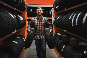 Male mechanic holding car tire in automobile store