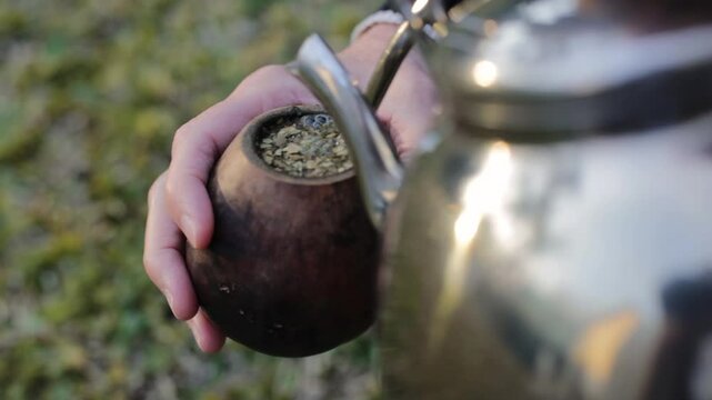 An adult woman preparing yerba mate tea with hot water, a traditional South American infusion. It is a typical social drink from Argentina, Uruguay, Brazil, and Paraguay	
