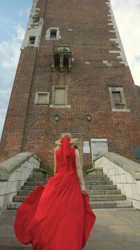 A woman in red dress walks up the steps to the Town Hall Tower. Vertical fottage in slow motion.