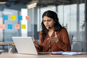 Angry woman yelling on online video call, support worker with headset working inside office using...