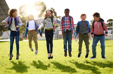 School kids, jumping and playing outdoor on grass with backpack for recess, learning break and fun activity. Students, friends and diversity group on lawn for playground game, education and energy