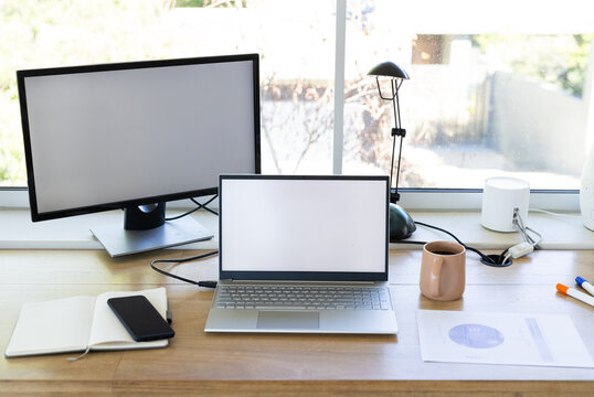At office, using laptop and monitor on desk with notebook and coffee mug, copy space