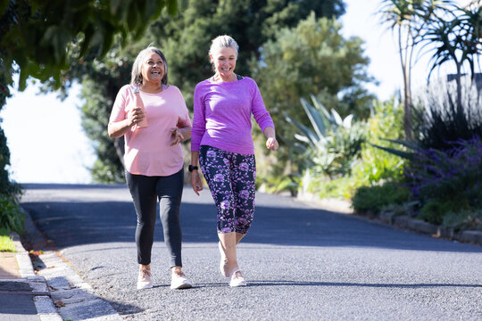Enjoying morning stroll, two senior multiracial female friends walking outdoors together