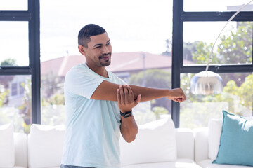 At home, Stretching arm, man in casual wear exercising indoors, smiling and staying active