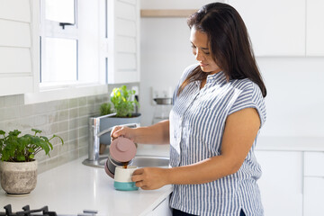 Pouring coffee from French press, woman enjoying morning routine in kitchen