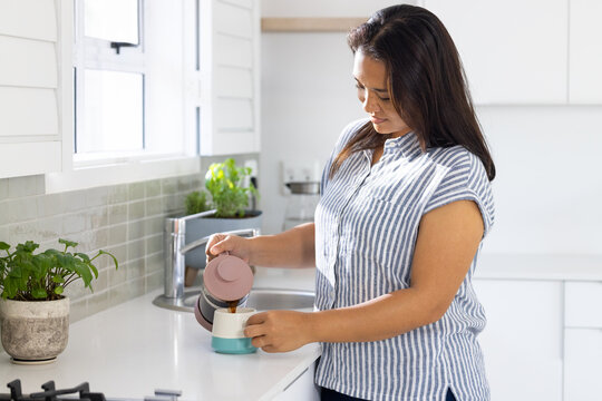 Pouring coffee from French press, woman enjoying morning routine in kitchen