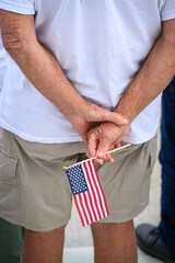 hands holding a small american flag behind back in honor