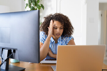 Working from home, woman with curly hair looking frustrated at laptop and desktop monitor
