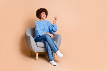 Full size photo of nice girl dressed knit sweater sit on armchair look directing at promo empty space isolated on pastel color background