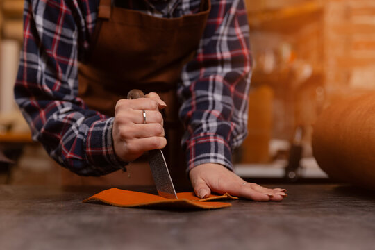 Young woman tailor cutting brown leather patterns in atelier workshop. Concept small business footwear industry, shoemaker