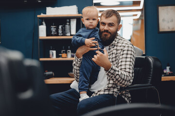 Young father supporting his little son before haircut at barber shop. Concept lifestyle dad and child boy barbershop