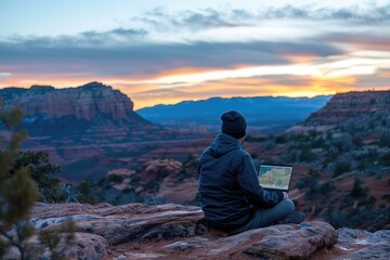 Fototapeta premium Man Using Laptop in Scenic Mountain Landscape at Sunset. Work Outdoors, Nature Inspiration