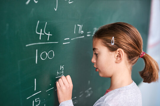 Girl, writing and math with chalkboard for equation, education or learning in classroom at school. Female person, child or young kid with fraction, numbers or problem solving for answer or solution