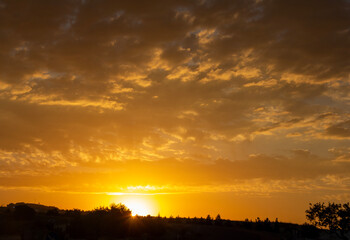 Golden sunset over a tranquil landscape, with warm hues painting the sky and soft clouds illuminated by the setting sun.