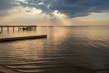 The Baltic Sea at sunset. A beautiful seascape with orange and gray clouds and a pier in the foreground. The city of Zelenogradsk and the embankment