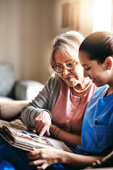 Elderly, woman and caregiver with photo album on sofa for memories, nostalgia and remember with...