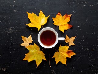 A warm cup of tea surrounded by vibrant autumn leaves on a rustic black table