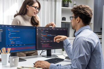 Woman colleague standing opposite to man programmer working on desk to discuss coding website...