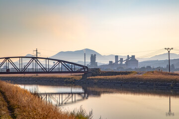 Industrial landscape. In the foreground is a water channel supplying the water power plant. In the background is a factory and power lines.