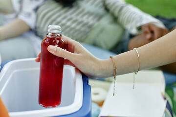 Close up on female hand taking cold berry lemonade out of cooler bag while having picnic with friends in park