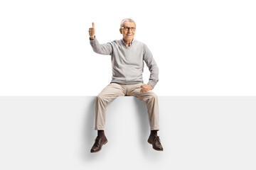 Happy elderly man sitting on a blank panel and gesturing thumbs up