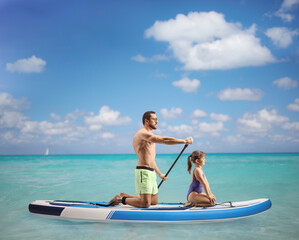 Man paddling a SUP board with a little girl in the sea