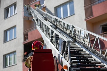 operator of fire truck with extended elevated ladder reaches up to residential building where...