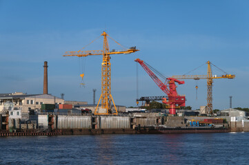 Obraz premium Port cranes on the pier of the commercial port on a summer evening. Bright colors in the rays of the setting sun. The border river Amur between Russia and China.