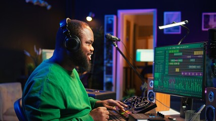 Young musician twisting knobs and mixing tunes with a console, following record settings on a digital software interface. Artist composer producing new music hits in his home studio. Camera B.