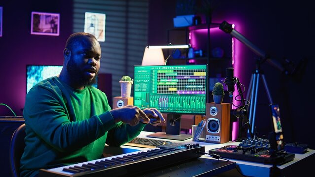 Musician doing online paid classes to help people play piano notes, teaching lessons from his home studio and recording video tutorials. Musical instructor playing midi controller keyboard. Camera B.