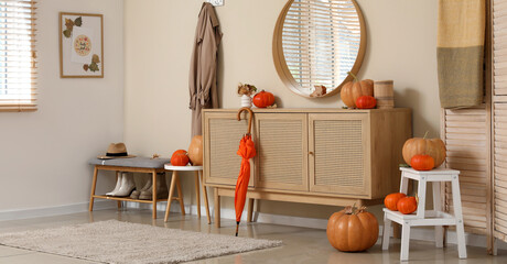 Mirror, chest of drawers and pumpkins with autumn leaves in interior of hallway