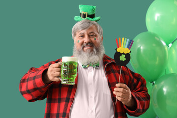 Mature man with beer and balloons on green background. St. Patrick's Day celebration