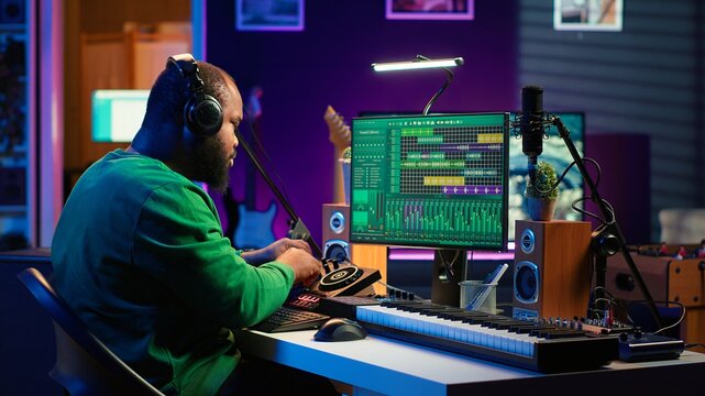 Confident music composer mixing sounds on digital audio software, creating a cool atmosphere in his home studio. Young cheerful producer composing new soundtracks with stereo gear. Camera A.