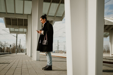 Side view of fashionable woman in coat using phone on train station.