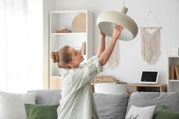 Young woman screwing light bulb into hanging lamp at home