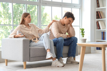 Young woman with her upset husband sitting on sofa at sexologist's office