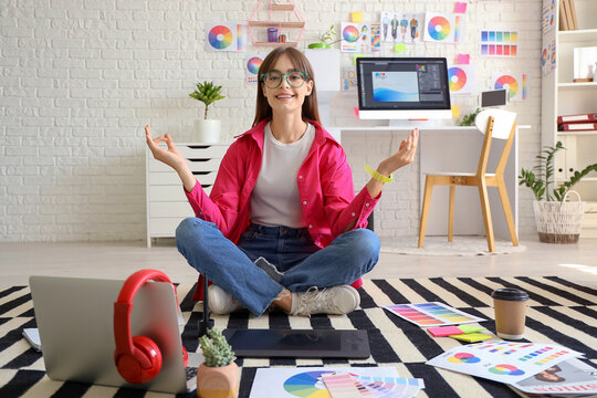 Female graphic designer meditating on floor in office - Powered by Adobe
