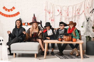 Cute happy children in different costumes with pumpkins dressed for Halloween party sitting on sofa...
