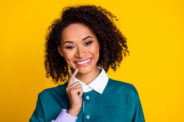 Portrait of toothy beaming nice girl with wavy hairstyle wear teal shirt holding finger on chin isolated on yellow color background