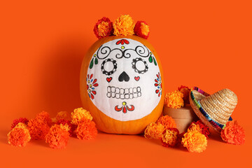 Pumpkin with painted skull, beautiful marigold flowers and mini sombrero on orange background. El Dia de Muertos