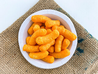 Puff  Snacks, tangy orange color, Popular Ready to eat crunchy and puffed snacks, salty in white ceramic bowl over white background.
