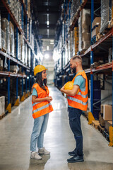 Two warehouse workers discussing tasks in the stockroom aisle