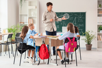 Male teacher with molecular model conducting Chemistry to little pupils in classroom