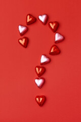 Question mark made of heart shaped chocolate candies on red background