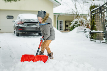 Adorable little boy helping to shovel snow in a backyard on winter day. Cute child wearing warm clothes playing in a snow. © MNStudio