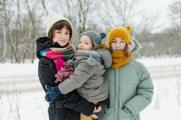 Two big sisters and their toddler brother having fun outdoors. Two young girls holding their sibling boy on winter day. Kids during winter break.