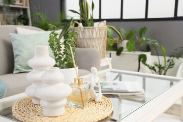 Reed diffuser with statuette, vases and plant on table in living room, closeup