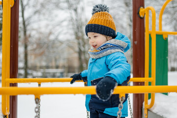 Adorable little boy having fun on a playground on snowy winter day. Cute child wearing warm clothes playing in a snow.