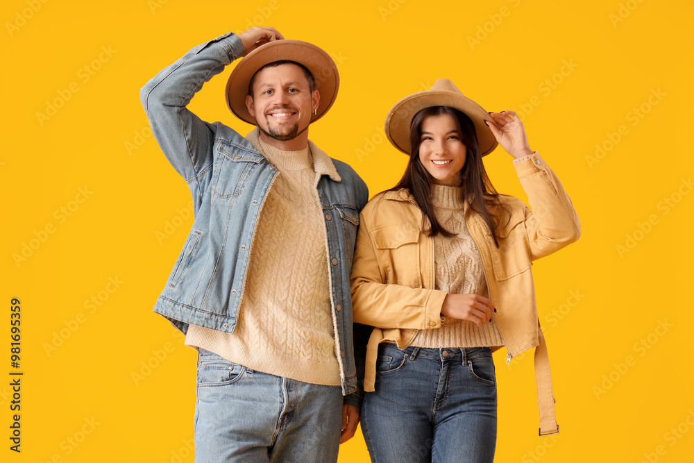 Wall mural Young couple in autumn clothes with hats on yellow background