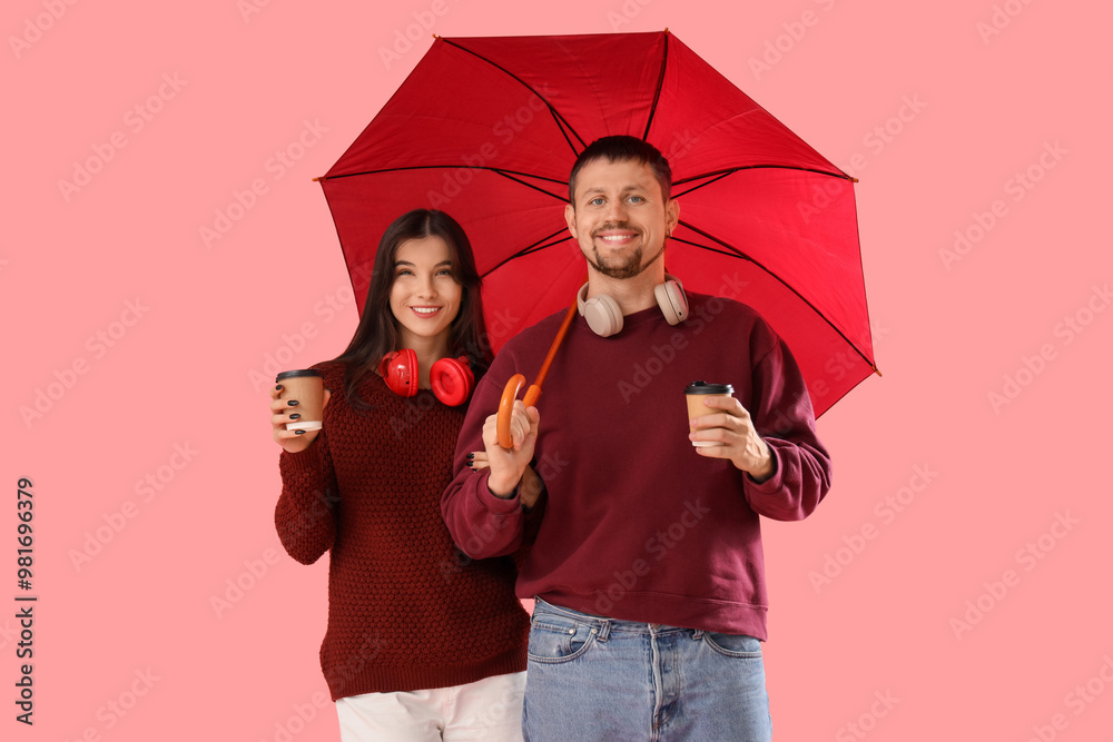 Wall mural Young couple in autumn clothes with umbrella and coffee cups on pink background